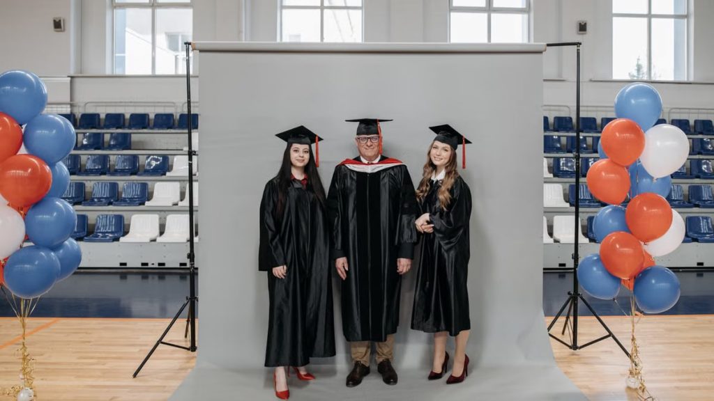 Group graduation portrait with caps and gowns in gymnasium setting.