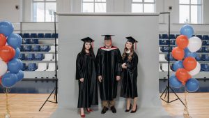 Group graduation portrait with caps and gowns in gymnasium setting.